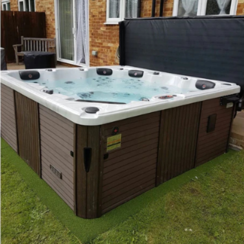 A lifestyle shot of the Vancouver 65-Jet 6-Person Hot Tub. You can see the brown panelling on the outside of the tub and a property behind it.